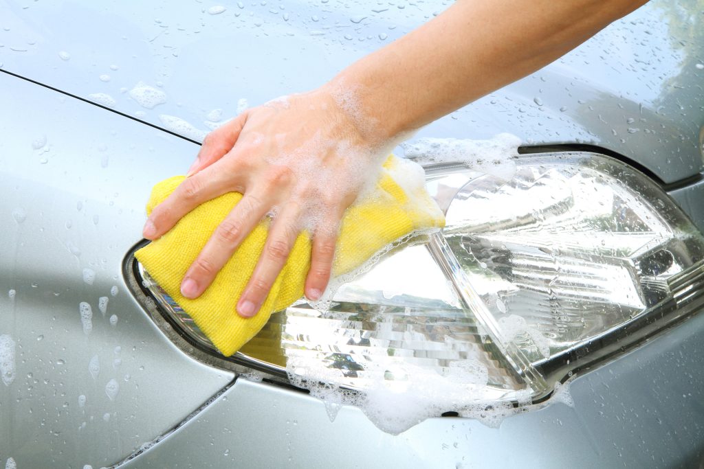 a hand washing headlight of the car in car wash shop.
