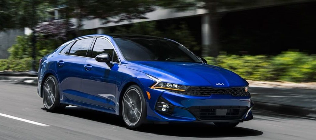 A blue 2023 Kia K5 on the city road.