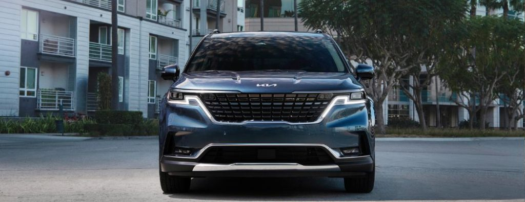 Front view of a 2024 Kia Carnival backdropped by a building