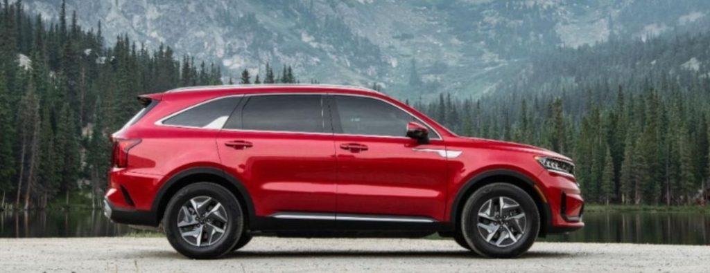 Side view of a red 2023 Kia Sorento Hybrid in front of the mountain.