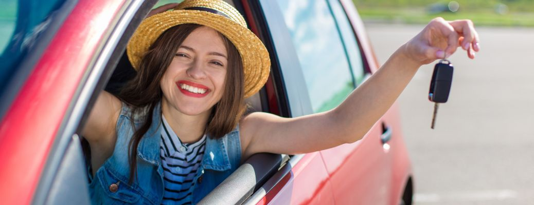 a smiling woman with her hand out the window of a car holding a key