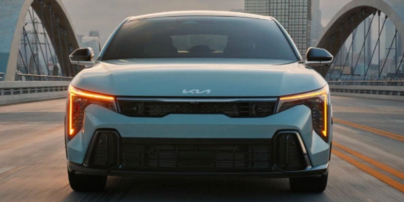 Front view of a light blue Kia car with bright orange daytime running lights, a dark grille, and a Kia logo above it.