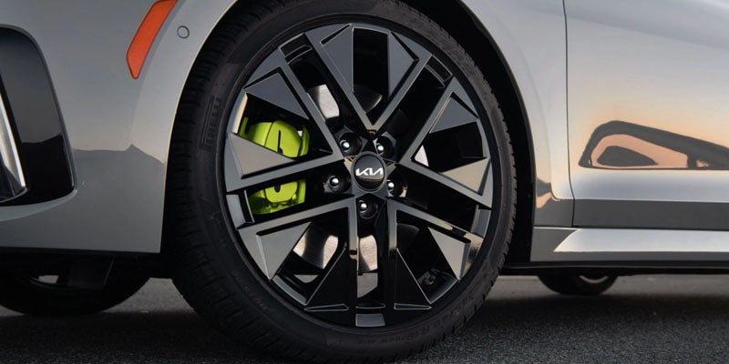 Close-up of a gray car's front wheel with black geometric spokes and bright green brake calipers.