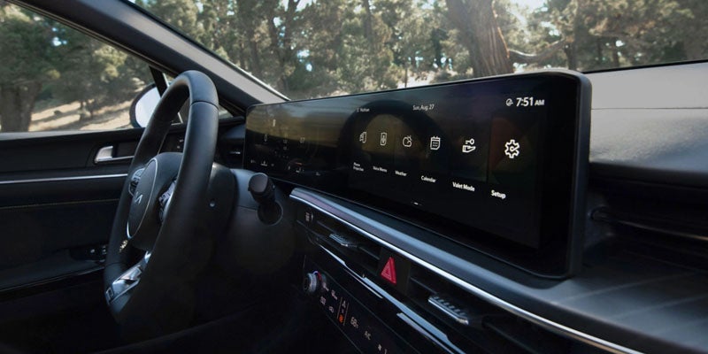 Interior view of a car showing a large infotainment screen with various app icons, dashboard, and steering wheel.