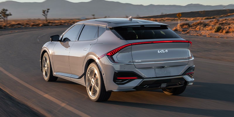 Rear view of a light gray Kia EV6 driving on a desert road with mountains in the background.