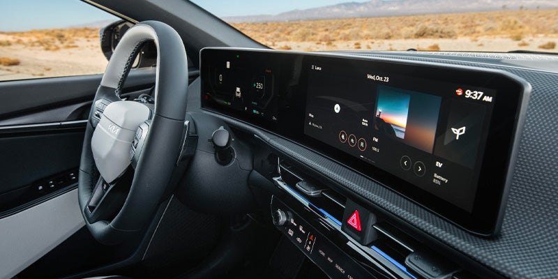 Interior shot of a car, showing the steering wheel and a wide digital display dashboard with navigation and media info.