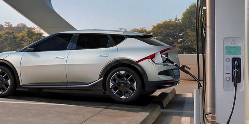 A gray electric car charging at a white charging station outdoors.
