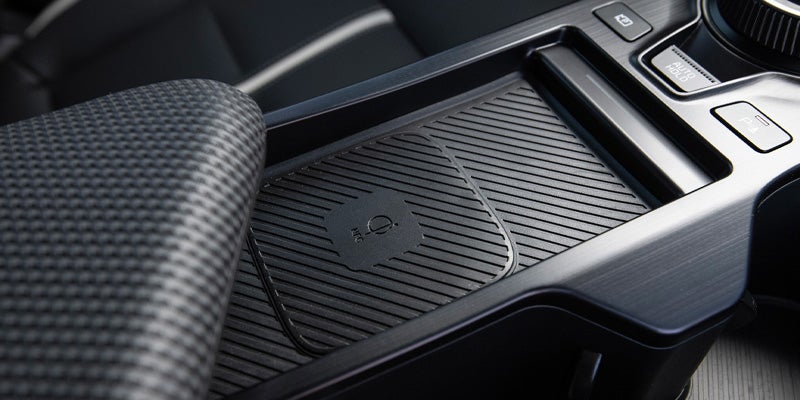 A close-up of a car's center console with a wireless charging pad and other buttons.