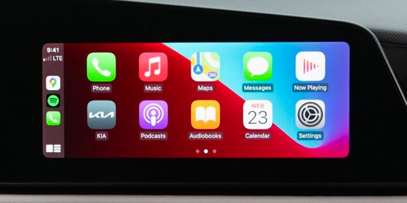 A car's infotainment screen showing CarPlay with app icons for Phone, Music, Maps, Messages, Now Playing, KIA, Podcasts, Audiobooks, Calendar, and Settings.