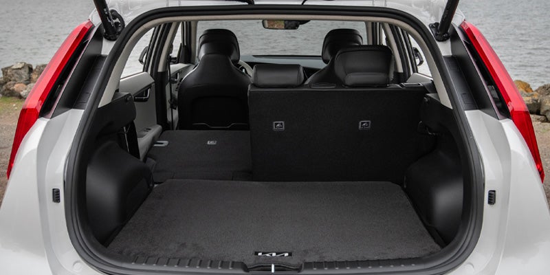 The back of a white EV with its trunk open, showing the rear seats folded down on the left and upright on the right.