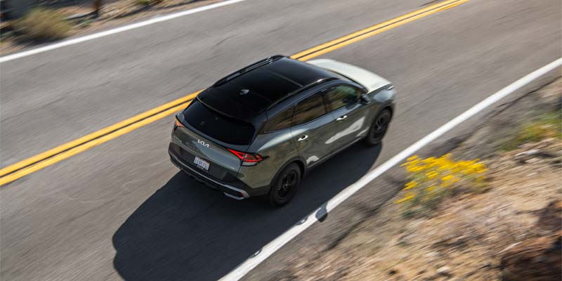 Aerial rear view of the 2025 Kia Sportage driving on a winding road.