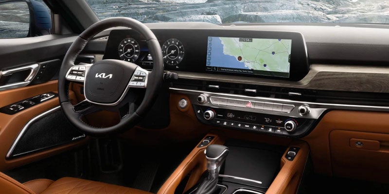 Car interior with a tan dashboard and black steering wheel. A wide screen shows a navigation map.