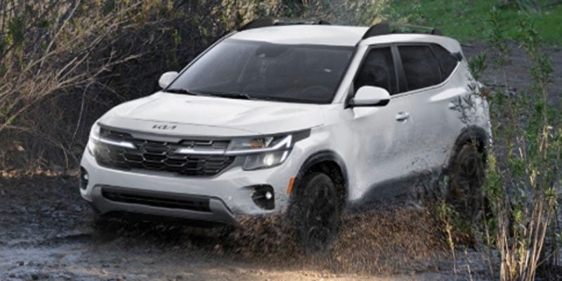 Side view of white SUV splashing through mud.
