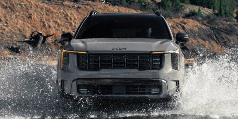 Three-quarter front view of a Kia Sorento parked on a dirt path with two people standing nearby.