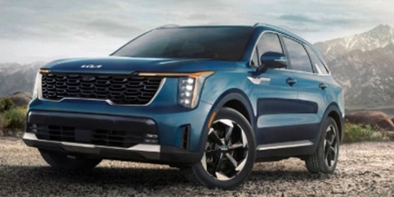 Front-three-quarter view of a blue SUV parked on gravel with mountains behind.