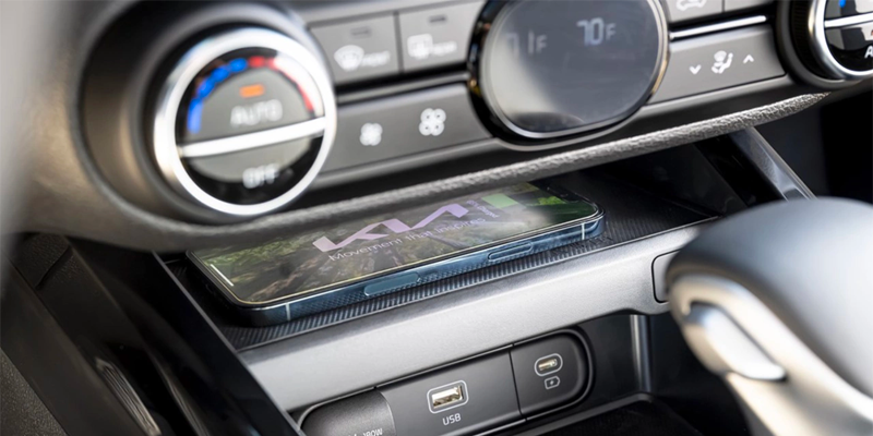 A smartphone with the Kia logo and "Movement that inspires" sits on a wireless charging pad in a car interior.