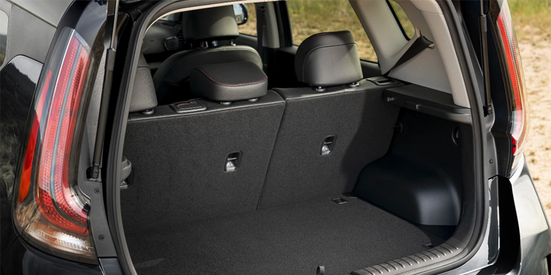 The open trunk of a black SUV shows a spacious black carpeted cargo area with the rear seats upright.