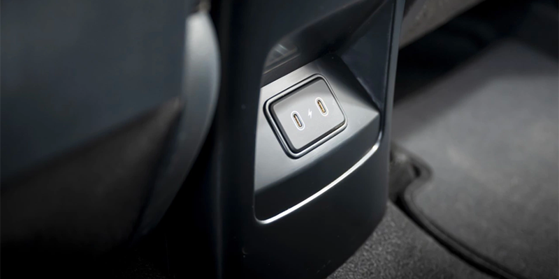 A close-up of a car's black interior, showing a charging port with two oval USB-C outlets and a lightning bolt icon.