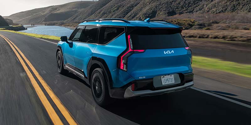 Rear view of a blue Kia EV9 driving on an open road.