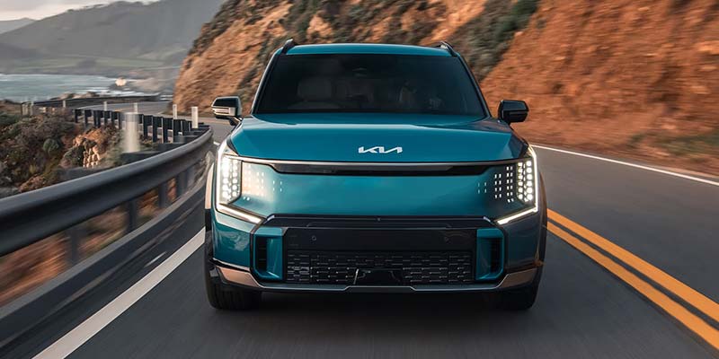 Front view of a blue Kia EV9 driving on a winding mountain road.