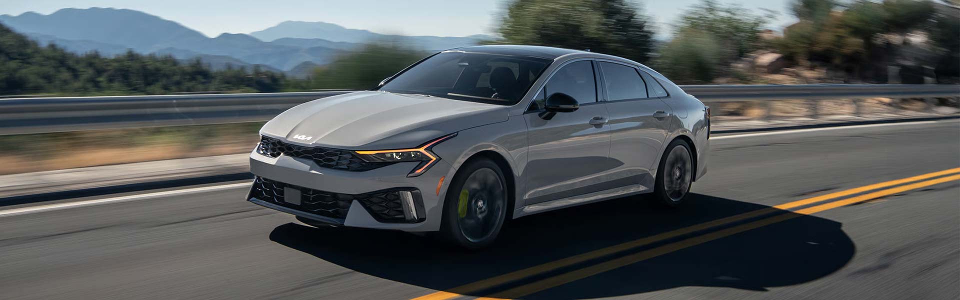 Gray Kia sedan driving on a highway with mountains in the background.