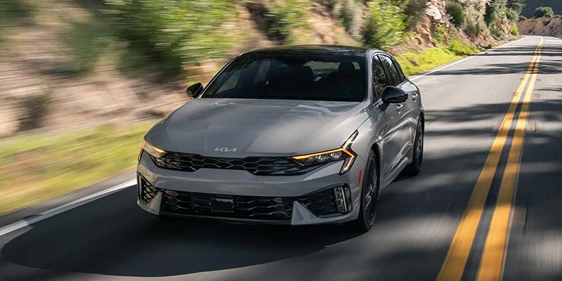 Gray Kia K5 driving on a winding mountain road.
