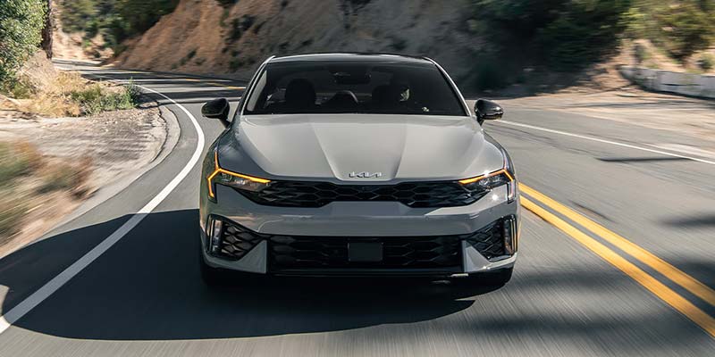 Front view of a Kia K5 driving through a curve.
