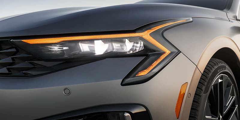 Front three-quarter view of a gray Kia K5 on a highway.