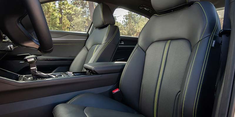 Interior of a car's front passenger seat and driver's seat, both black with neon yellow stitching patterns.