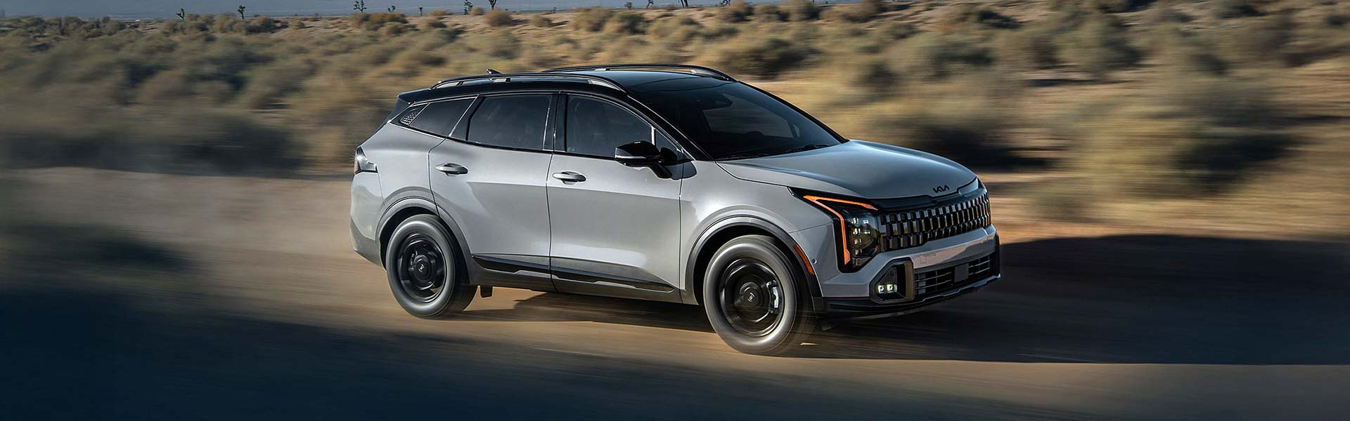 Silver 2026 Kia Sportage driving on an open desert road.