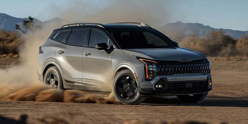 2026 Kia Sportage driving through dusty off-road terrain.