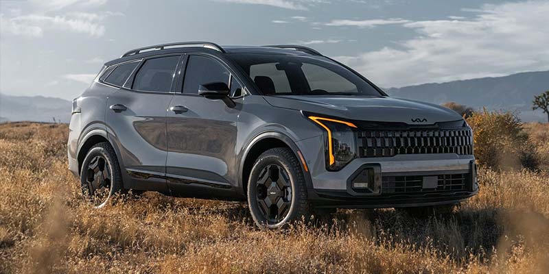 2026 Kia Sportage parked in a grassy field with mountains behind.